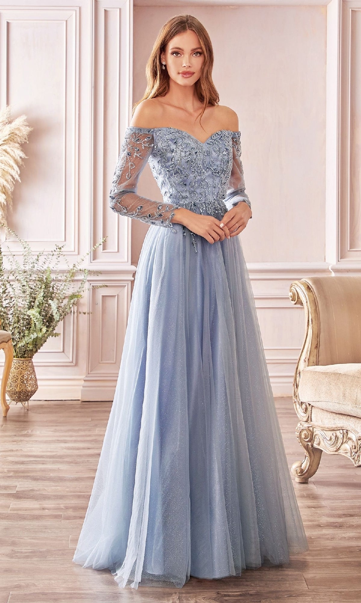 A woman indoors wears the Ladivine CD0172, a light blue off-the-shoulder long prom dress with lace-detailed bodice and sheer long sleeves.
